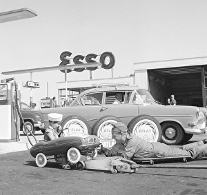 Service station of the 1950s. A boy in his pedal car has it serviced at an Esso petrol station
