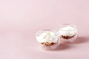 Two servings of tiramisu in a glass cup on a beige background