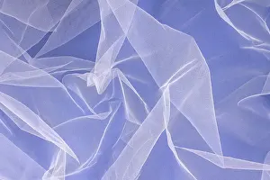 Sheer tulle fabric arranged in soft folds on a blue background