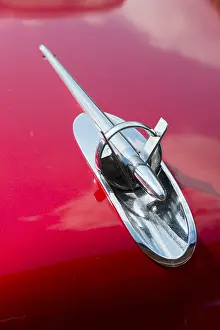 A shiny chrome radiator grille on the bonnet of a red classic car