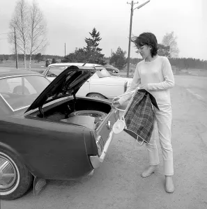 Shopping in the 1960s. A lady has parked her car at the supermarket and takes out her shopping cart on the parking lot