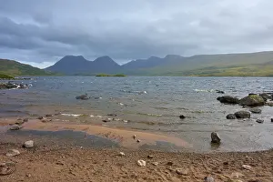 Shores of a lake with waves and mountains in the background under cloudy sky