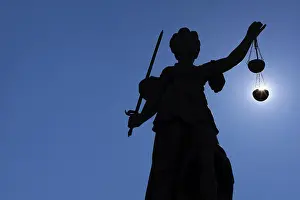 The silhouette of the Justitia statue on the Romerberg in Frankfurt am Main is silhouetted against the sun