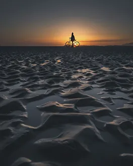 Silhouette of a person with a bicycle on a beach during a picturesque sunset