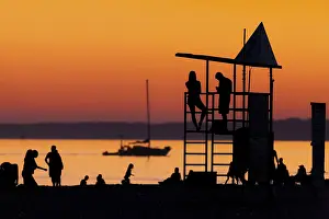 Silhouetted figures against an orange sunset on the beach with a lifeguard tower