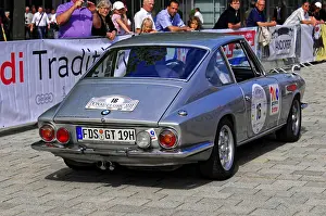 A silver classic car at a rally surrounded by an audience