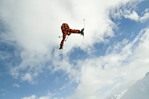Skier jumping in front of a blue sky with a snow-covered mountain range behind