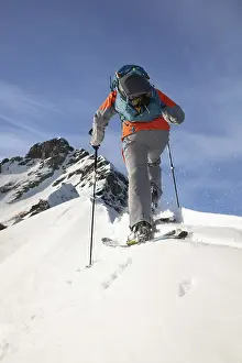 A skier wearing gear ascends a snowy mountain with ski poles