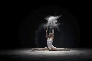 Slender girl sitting in split in cloud of white dust studio shot