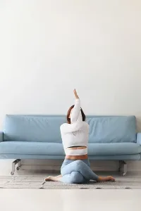 Slim female in sportswear bending aside while practicing yoga near sofa at home