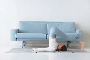Slim female in sportswear bending aside while practicing yoga near sofa at home