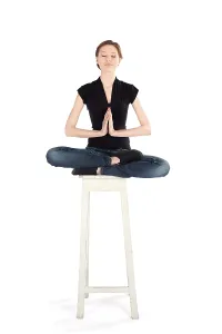 Slim woman sitting on high stool doing yoga meditation technique isolated on white background