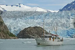 Small boat in front of the ice front of a glacier calving into the sea