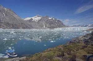 A small boat moored on a clear fjord in front of an impressive mountain and glacier landscape