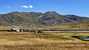 Framed Print : Small houses in front of a hill and mountain landscape under a blue sky