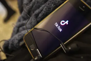 Smartphone displaying the TikTok app logo with tangled earbuds resting on it