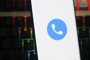 A smartphone displays a blue phone app icon against a white background over a colorful keyboard