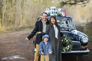 Smiling adult man and woman with boy in warm clothes standing at vintage car with Christmas presents