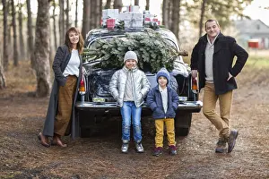 Smiling adult man and woman with kids in warm clothes standing at vintage car with Christmas presents