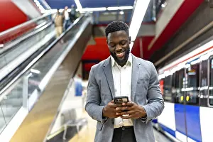 Smiling businessman using a smartphone while waiting for a train at an urban subway station