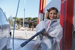Smiling girl using a high pressure hose at a car wash