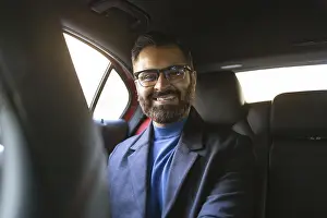 Smiling Indian businessman wearing glasses and winter attire seated in a car