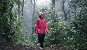 A smiling woman in a red raincoat hiking through a lush