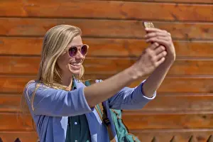 Smiling woman taking selfie in front of wooden wall during weekend trip adventure she shares online with her friends