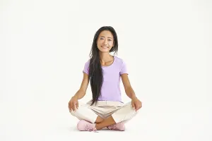 Smiling young asian woman sitting sitting on floor with legs crossed looking to camera isolated over white background