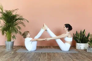 Smiling young woman and little girl practicing yoga on mat in cozy living room