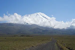 A snow-covered mountain under blue sky with a path in the foreground