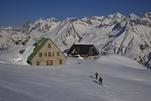 Snow-covered mountain huts with ski tourers in front of the impressive mountain panorama of the Allgau main ridge