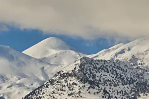 Snow-covered mountain peaks silhouetted against a clear blue sky with a few clouds