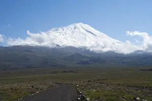 A snow-covered mountain rises majestically under a clear blue sky with scattered clouds