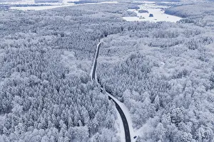 Snow-covered road leads through a vast winter forest