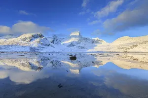 Snow-covered steep mountains reflected in fjord