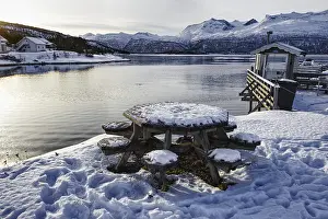 Snow-covered table and benches by the lake with mountains in the background