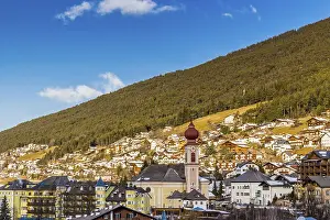 Snowy alpine village in Italy illuminated by sun with mountains in the background