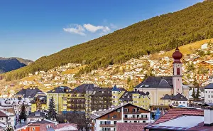 Snowy alpine village in Italy illuminated by sun with mountains in the background