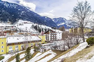 Snowy alpine village in Italy illuminated by sun with mountains in the background