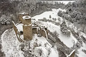 Snowy castle ruins in a wintry landscape with forest and hills
