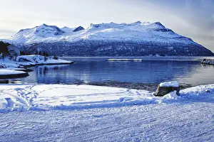 Snowy coastal landscape with mountains by the water