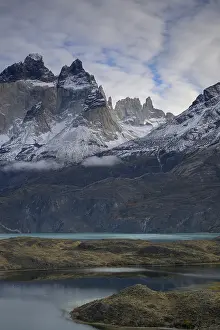 Snowy mountains near a turquoise lake under a cloudy sky