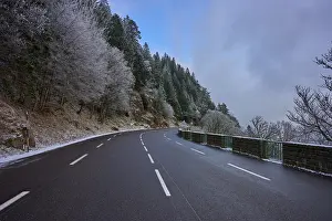 Snowy road snaking through a wintery forest with frost-covered trees