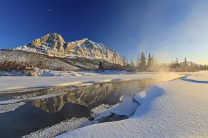 Snowy steep mountains reflected in frozen river