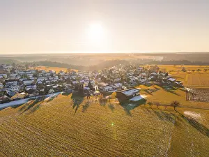 A snowy village in the light of the sunrise with surrounding fields