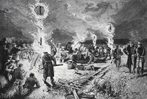 Soldiers gather around several campfires at night
