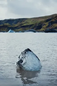 Solitary iceberg floating in calm waters with hills in the background