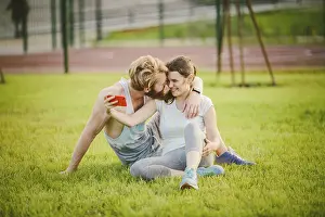 Sport and technology. Young in love heterosexual Caucasian couple resting after workout outdoors in park on lawn