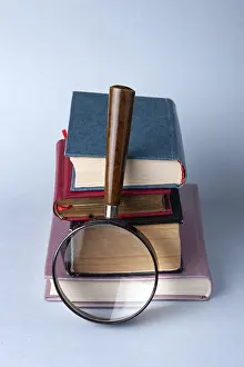 A stack of hardcover books and a magnifying glass on a blue background